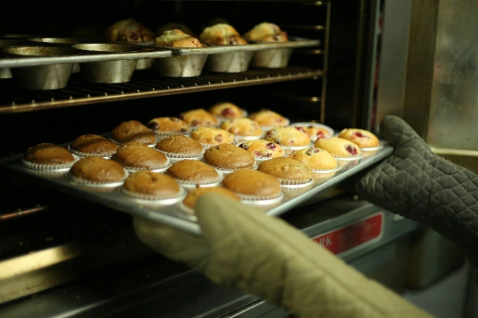 person takes a tray of muffins out of an oven